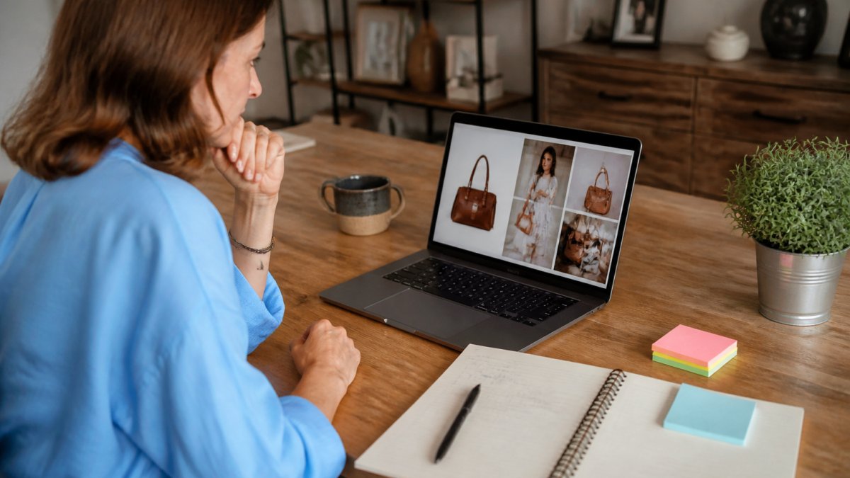 Small business owner at a desk reviewing AI-generated ad copy and images on a laptop screen, with marketing notes and coffee nearby